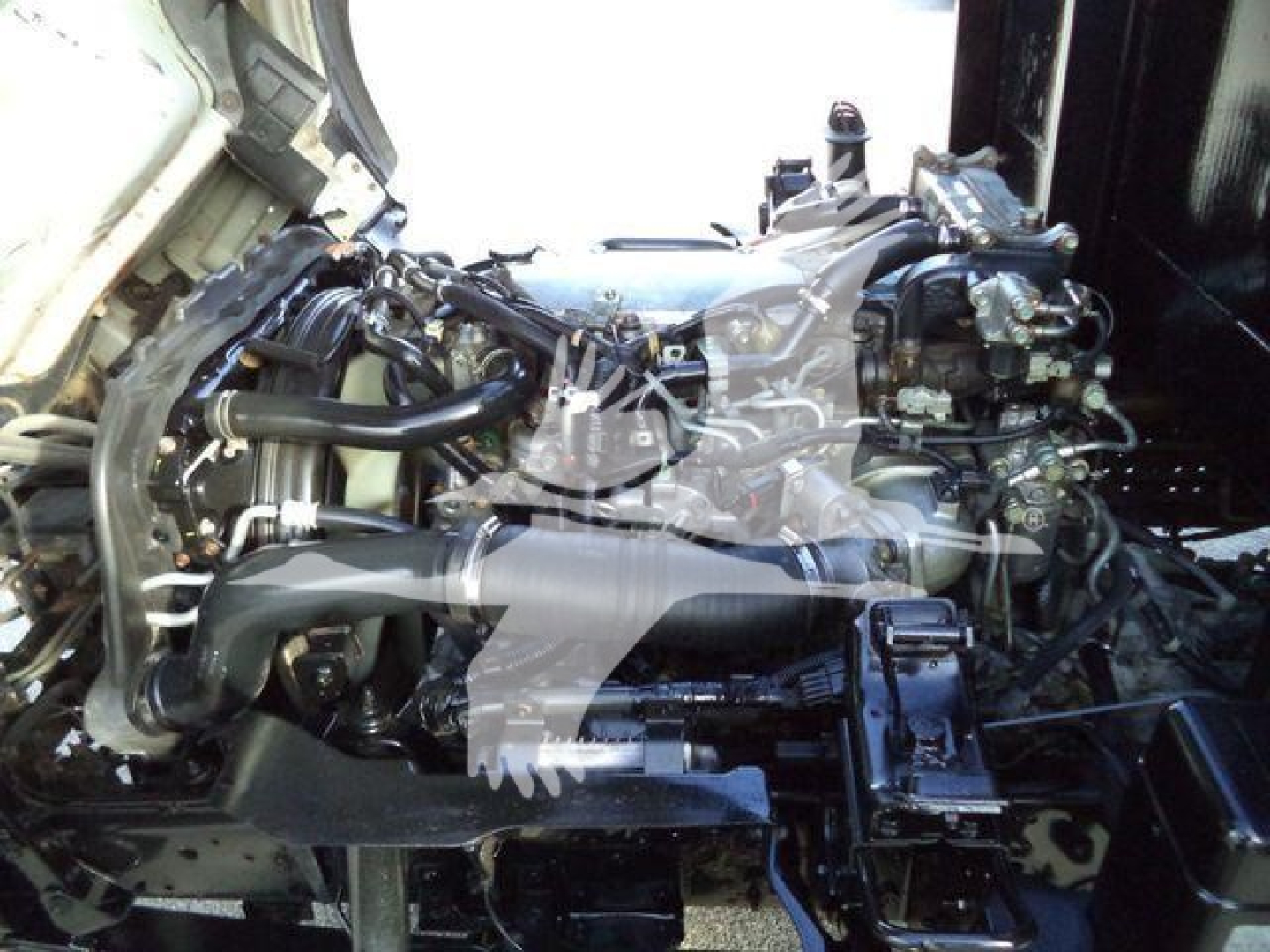 Isuzu NPRR engine bay showing compact turbo diesel engine with hoses and components visible.
