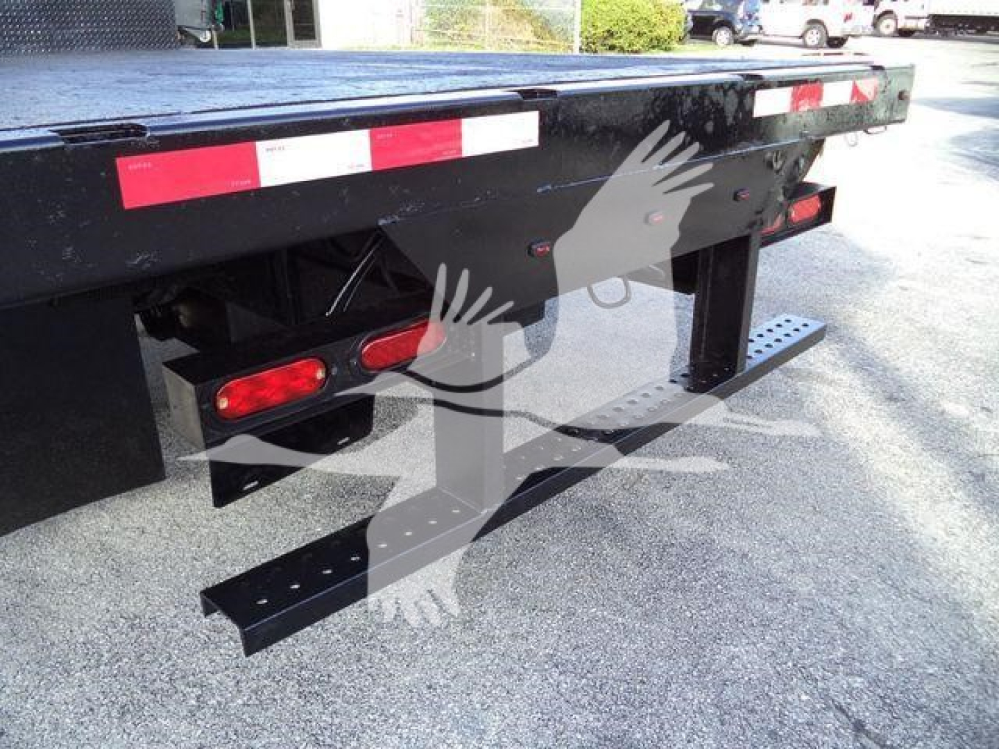 Isuzu NRR flatbed truck rear view showing bumper reflectors, side steps, and loading platform edge with safety markings.