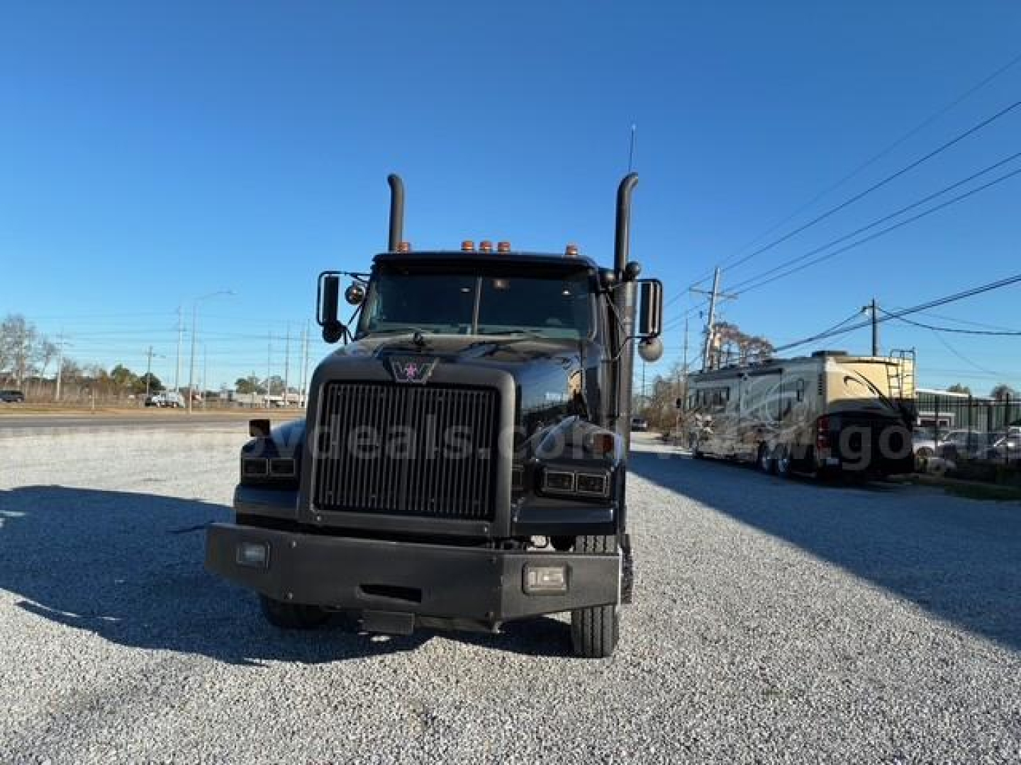 Front view of a black 2008 Western Star 4900 SA truck with large grille, dual tall exhaust stacks, and amber roof lights in a gravel lot.