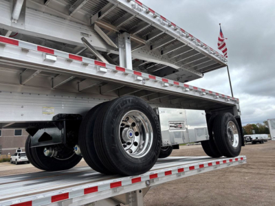 Flatbed trailer underside and wheels showing dual rear axles and metal decking with reflective red/white tape.