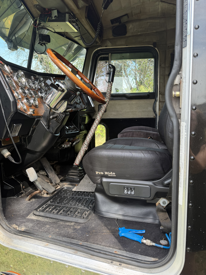 Truck cab interior of a Peterbilt 379X showing driver seat, steering wheel, dashboard, pedals, and floor mats.