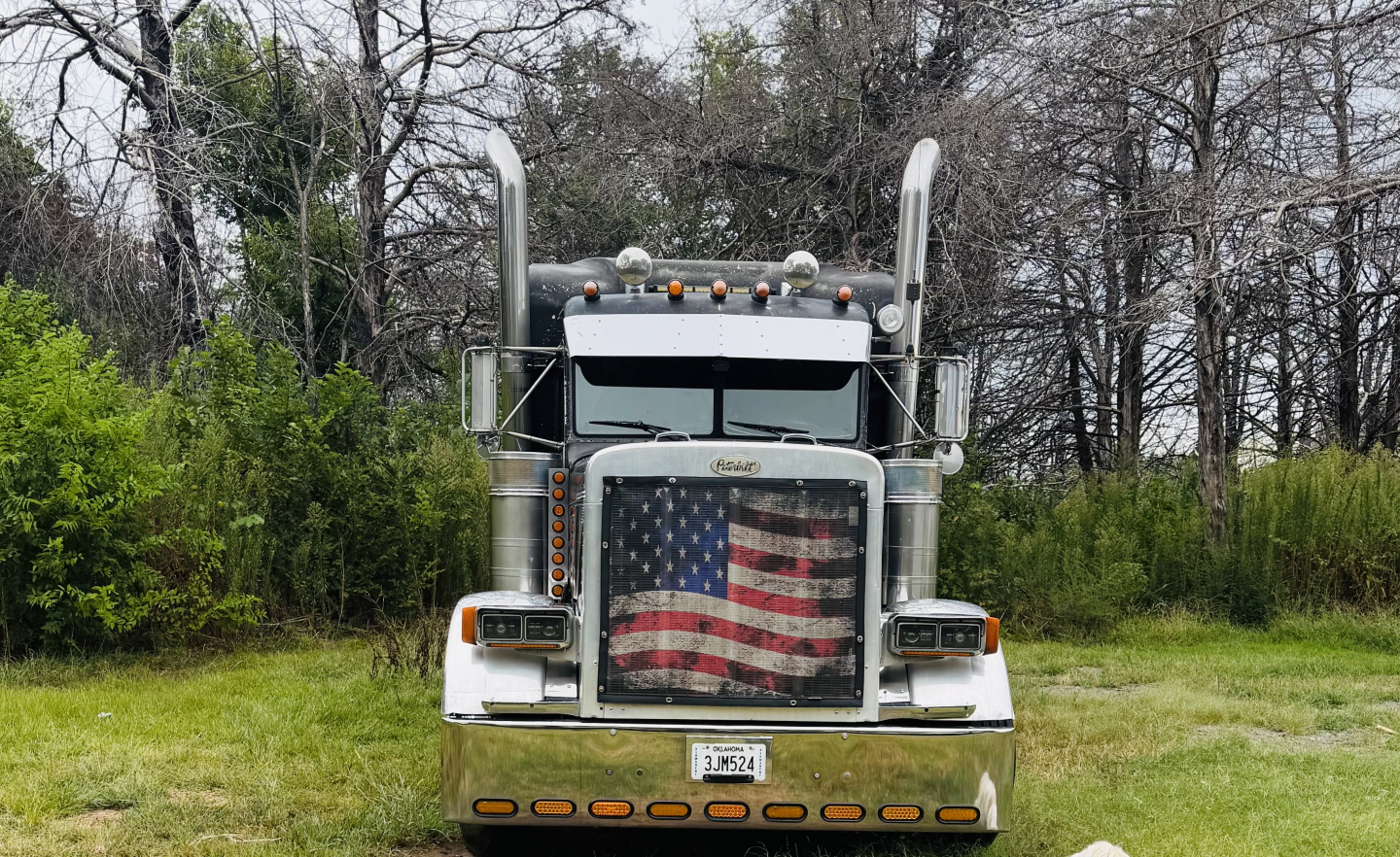 Peterbilt 379X conventional sleeper truck front view with American flag grille, dual vertical exhaust stacks, and license plate visible.