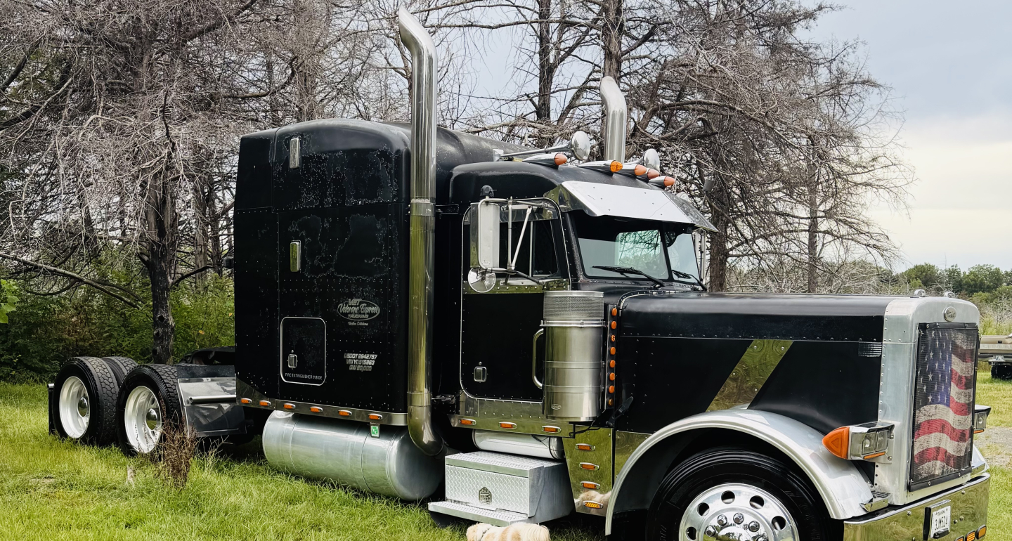 Peterbilt 379X conventional sleeper truck shown from front-right side with black cab, chrome exhaust stacks, large chrome bumper, and dual rear axles.