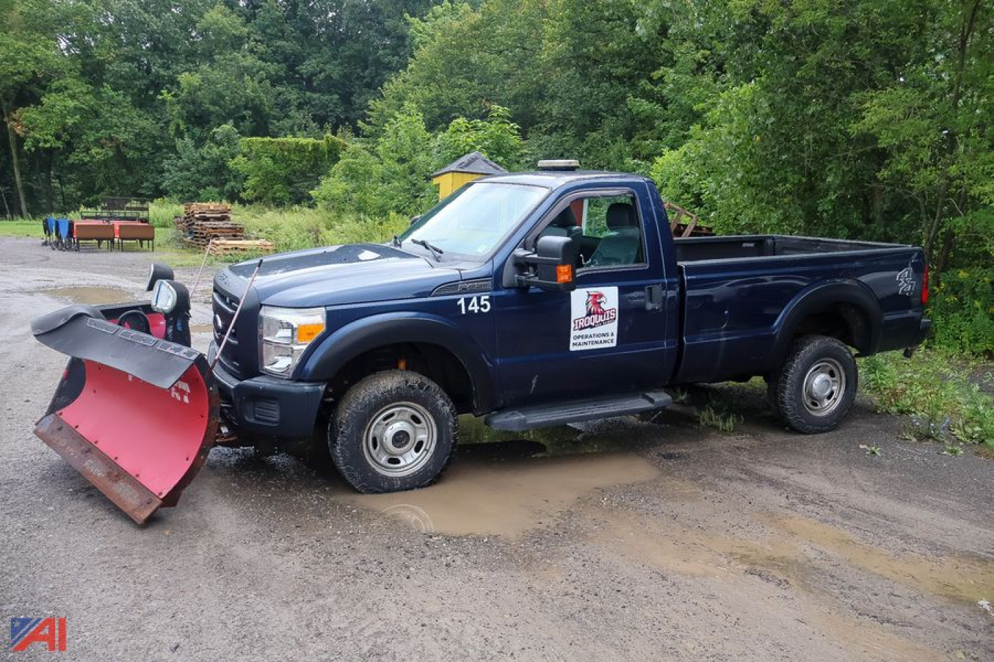 Ford F-350 Super Duty pickup with plow attachment and salt-and-pepper water on ground, side badge 145, two-tone blue truck in yard