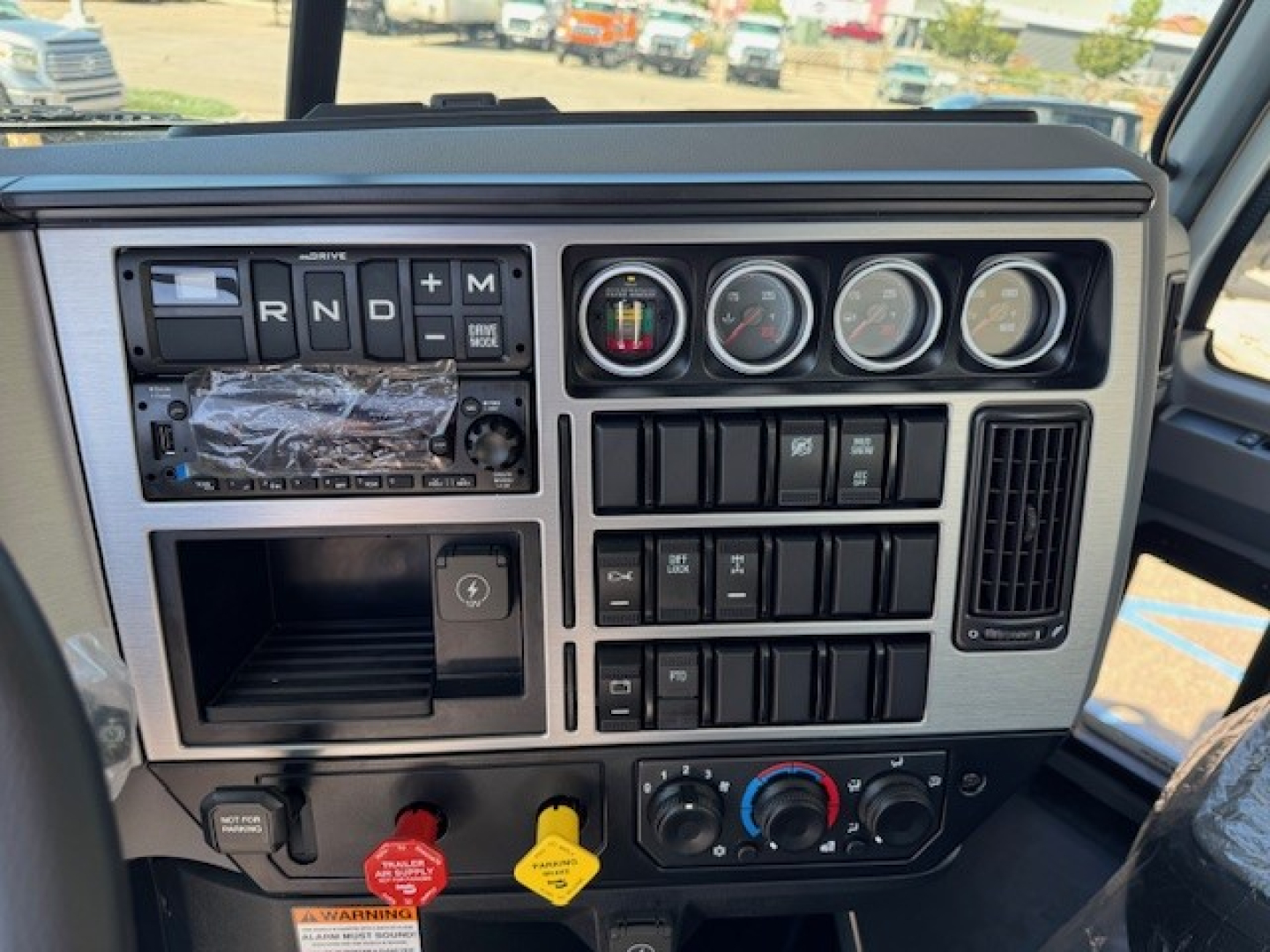 Dash of 2026 Mack PI64 dump truck showing gear selector R N D P, multiple gauges, switches, and climate controls in center console.