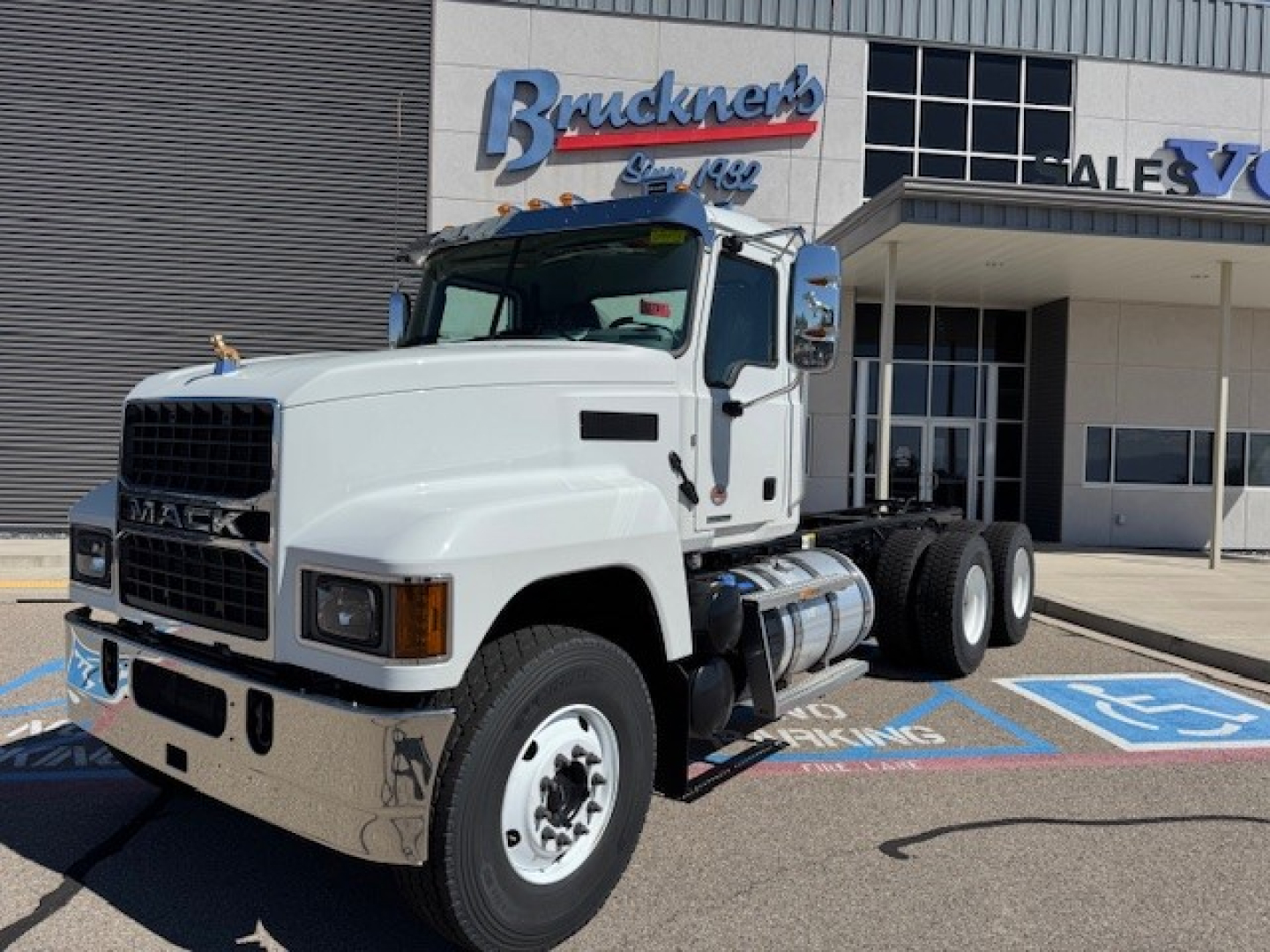 Mack PI64 dump truck in white color shown in front view with chrome bumper and dual rear axles, parked in a lot near a dealership.