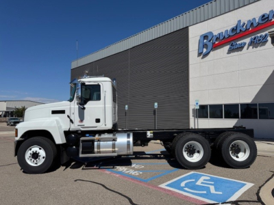 2026 Mack PI64 dump truck side view with white cab and dual rear axles parked in front of a dealership, visible text on building says 'Brunkner' (partially).