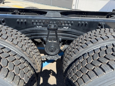 Mack PI64 chassis showing tandem rear axle with dual large off-road tires and drive belt pulley, view from between wheels