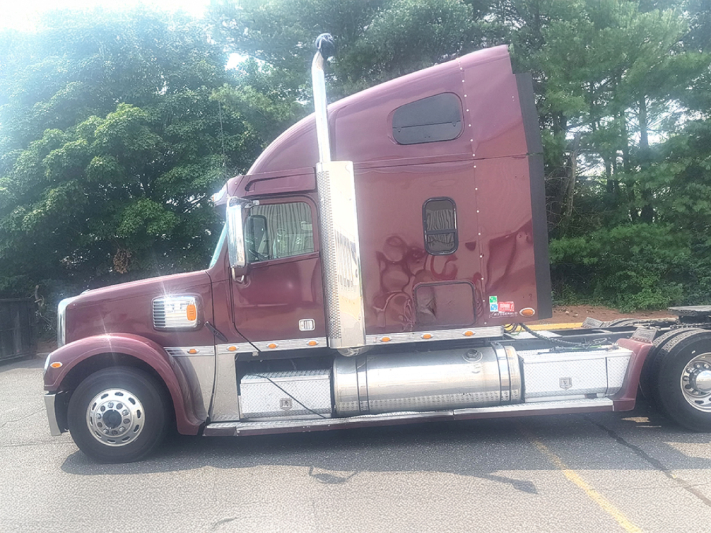 Truck cab exterior of a maroon 2016 Freightliner Coronado with chrome fuel tanks and vertical exhaust, side view showing sleeper cab and wheels.