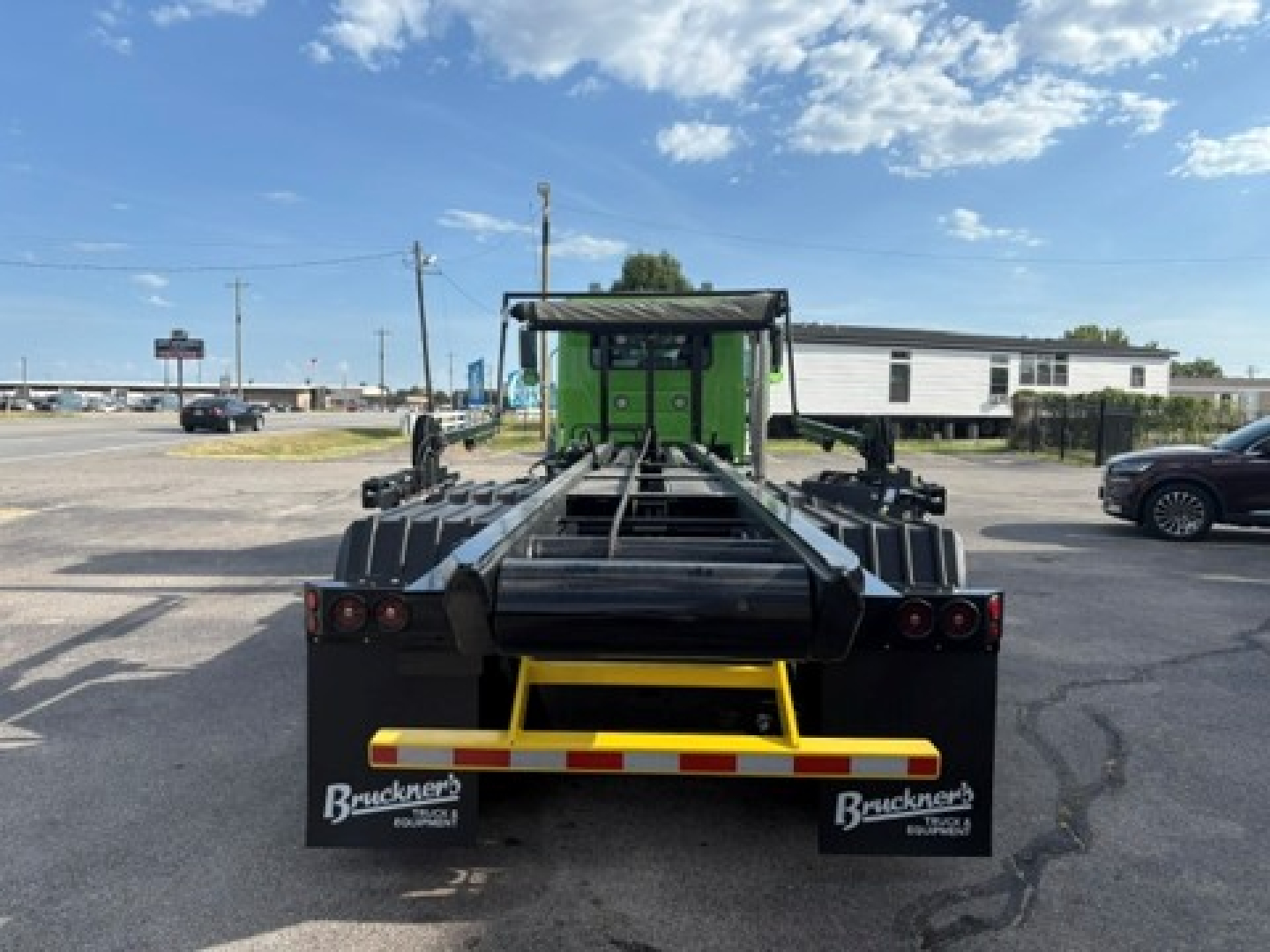 Rear view of a green Mack GR64F roll-off truck chassis showing black winch frame and yellow rear bumper with Brackner’s branding mud flaps.