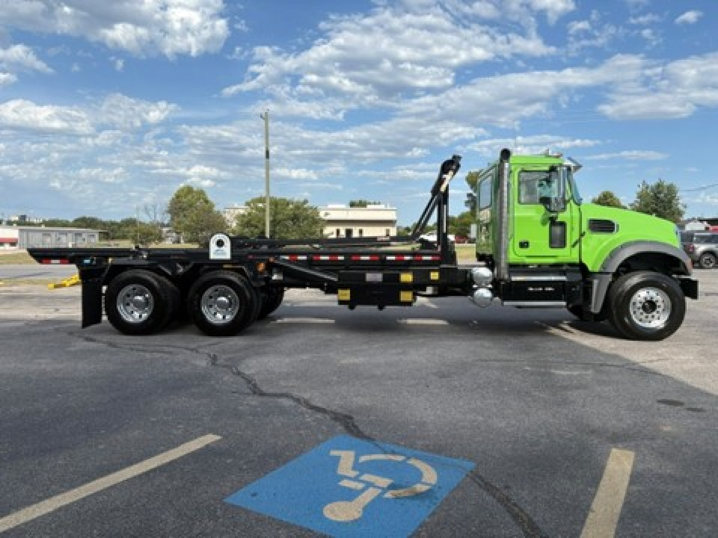 Green Mack GR64F roll-off truck side view showing long flatbed and rear axles with hydraulic crane arm attachment.
