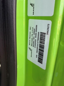 Label on green Mack GR64F showing VIN 1M2GR3GC4TM050589, stock 69477, model MACK TRUCKS INC, CHS: 9 99 8 5? etc. Barcode and serial numbers visible.
