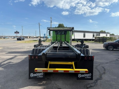 Rear view of a green Mack GR64F roll-off truck chassis showing black winch frame and yellow rear bumper with Brackner’s branding mud flaps.