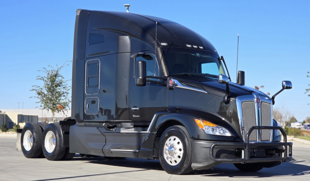 Kenworth T680 conventional sleeper tractor in dark color with aerodynamic cab, front bumper guard, dual rear axles, daytime running lights.