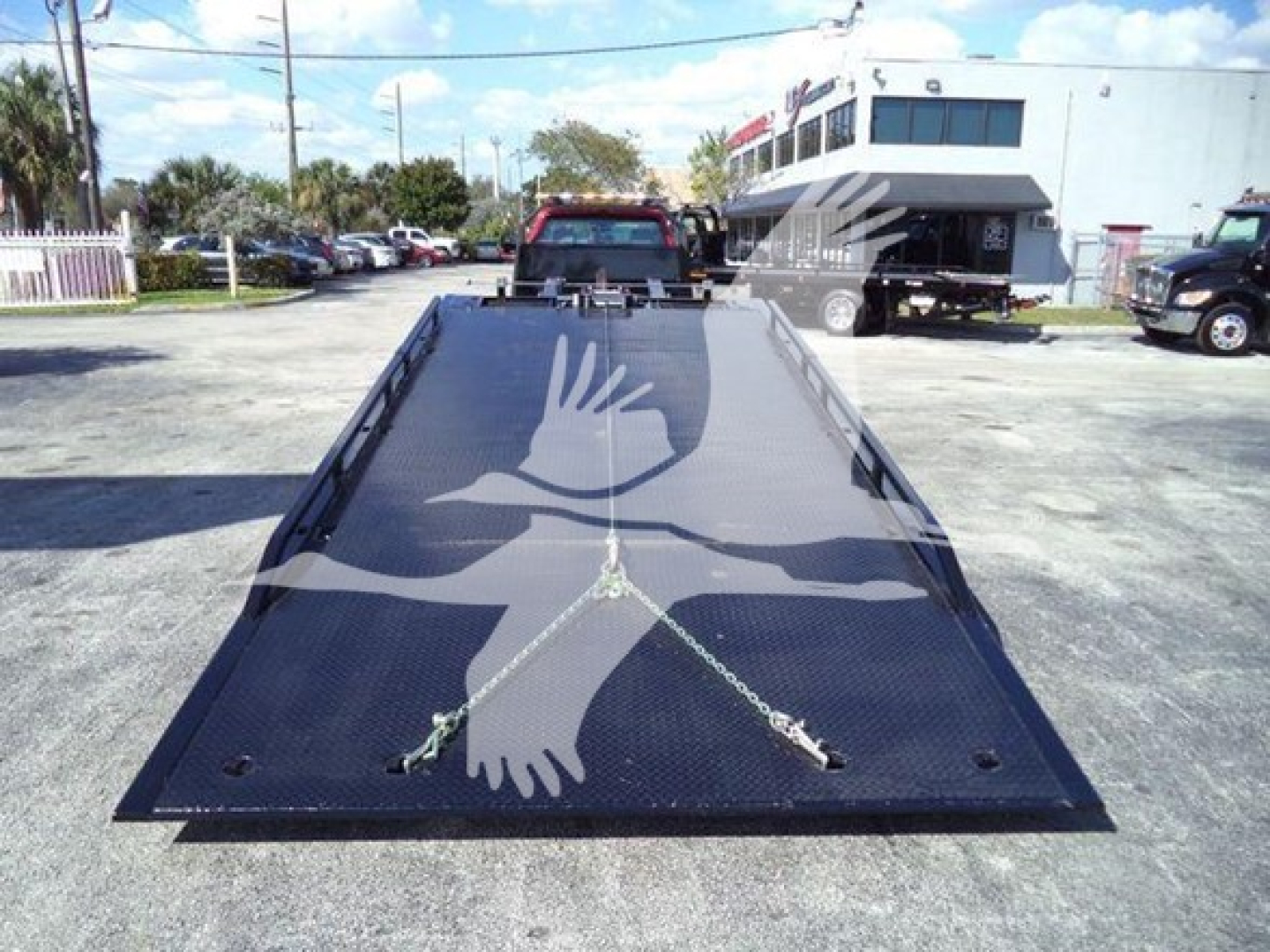 Flatbed tow truck bed with chevron pattern and tie-down chains, rear view of a 2023 Chevrolet Silverado 6500HD rollback on a dealership lot