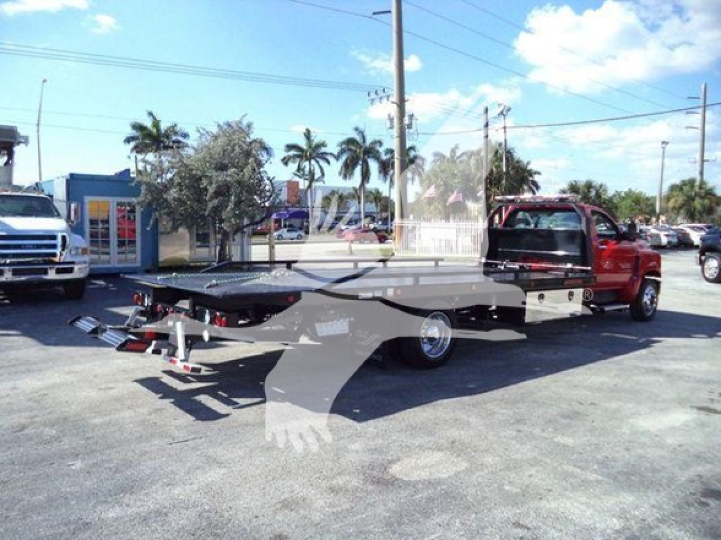 Flatbed tow truck with Chevrolet Silverado 6500HD in background, showing rollback bed and extended wheel lift.