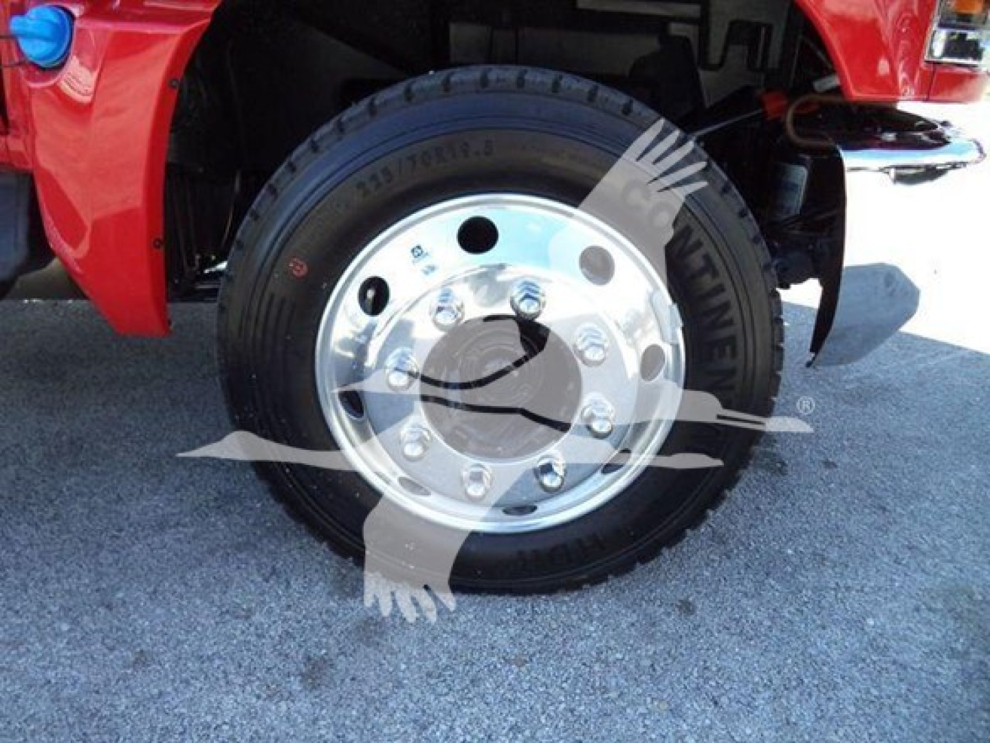 Front wheel and chrome hub of a red Chevrolet Silverado 6500HD rollback truck showing tire and polished steel wheel.