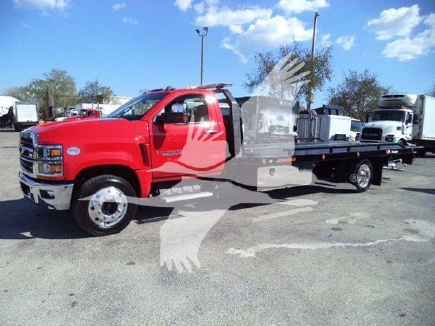 Red Chevrolet rollback tow truck with extended flatbed, cab and chassis visible, dealership lot in background.