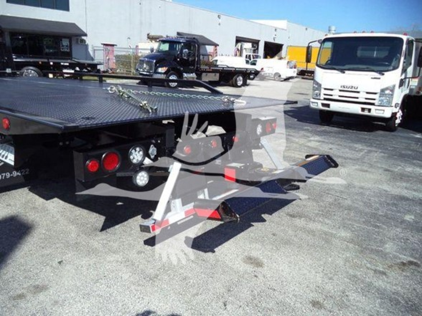 Truck rollback equipment with hydraulic bed and towing ramp; visible label text includes small circular lights and chain on bed.