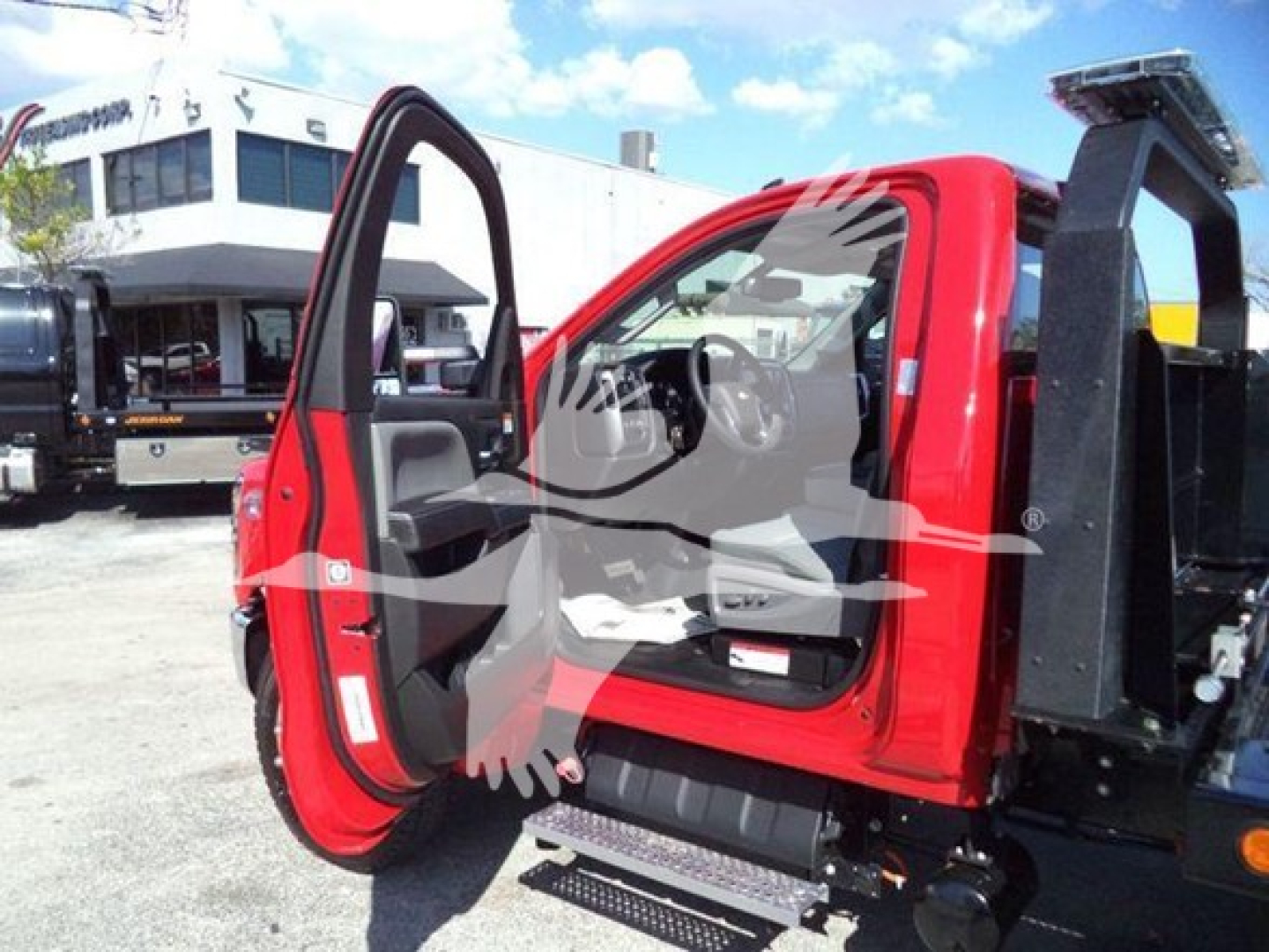 Truck cab open door showing red Chevrolet Silverado 6500HD rollback body with black equipment in background and clear sky