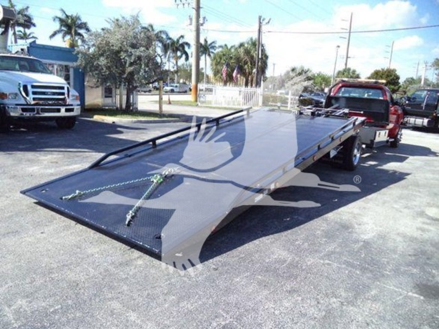Truck-bed rollback trailer on a dealership lot showing a low-profile steel flatbed with ramp, attached to a Silverado 6500HD.