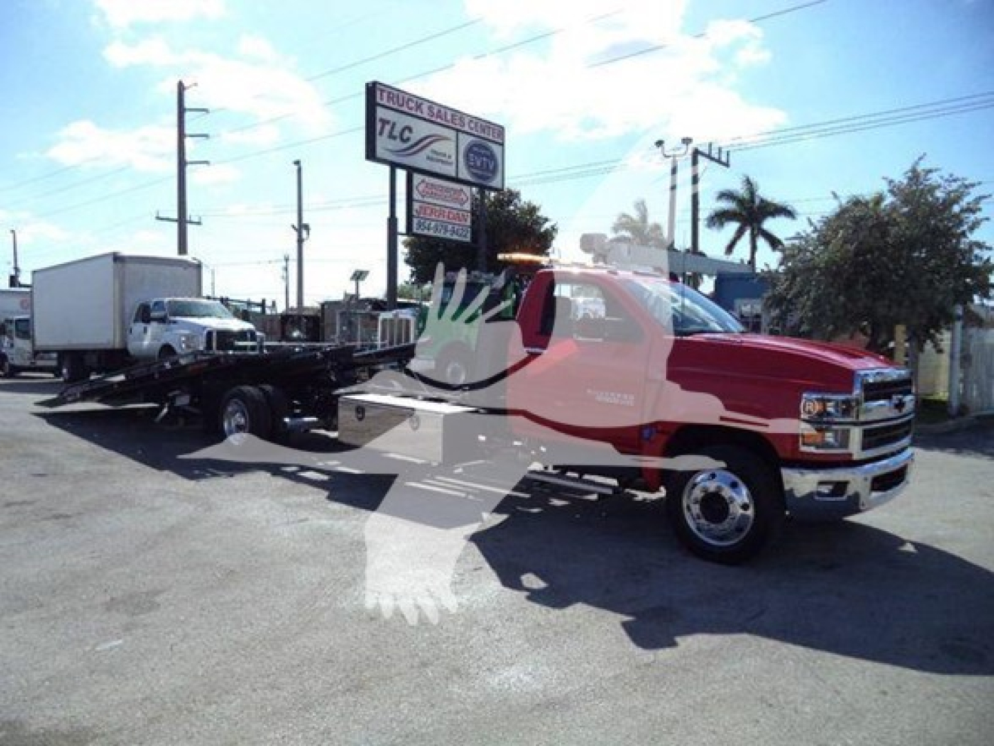 Truck rollback tow truck with red cab and black flatbed in a lot; Chevrolet emblem on front grille.