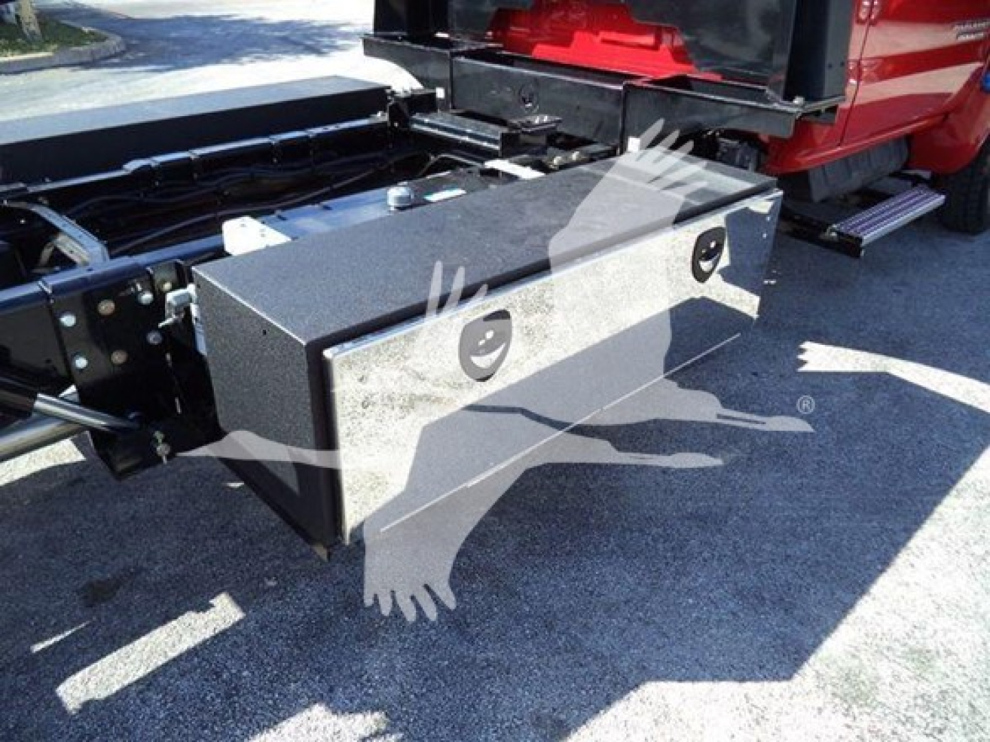 Truck chassis with a metal rectangular toolbox mounted behind cab showing two circular access holes and mounting brackets.