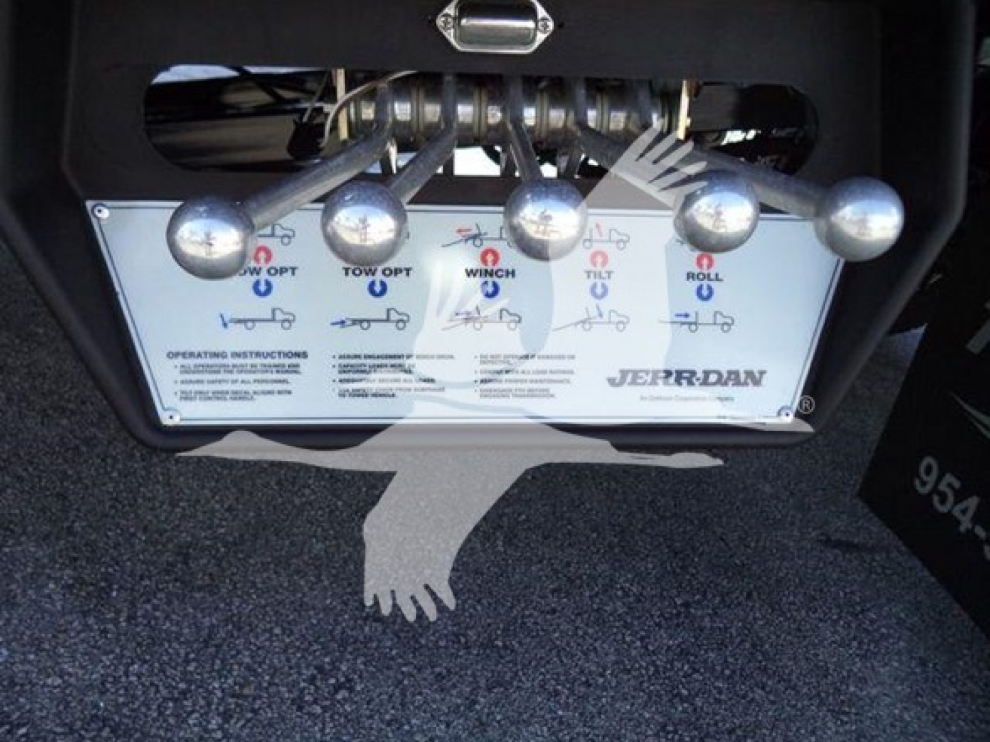 Truck control panel showing tow/winch/tilt/roll controls with labels and icons, brand 'Jerr-Dan' visible, levers and graphics on a metal plate.
