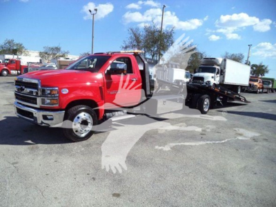 Front left angle of a red 2023 Chevrolet Silverado 6500HD rollback tow truck with a flatbed in a dealership lot.