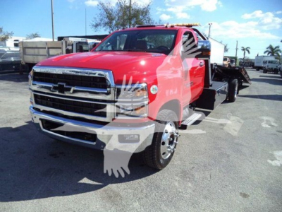 Truck image showing a red 2023 Chevrolet Silverado 6500HD rollback tow truck front-left view with chrome grille and black wheels.