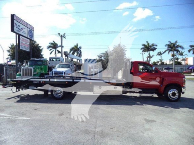 Flatbed tow truck with a red cab and long black flatbed, Chevrolet Silverado 6500HD title text overlaid by watermark, dealership lot in background.