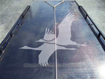 Platform bed of a rollback truck with diamond plate surface and a large white eagle decal in the center, viewed from above.