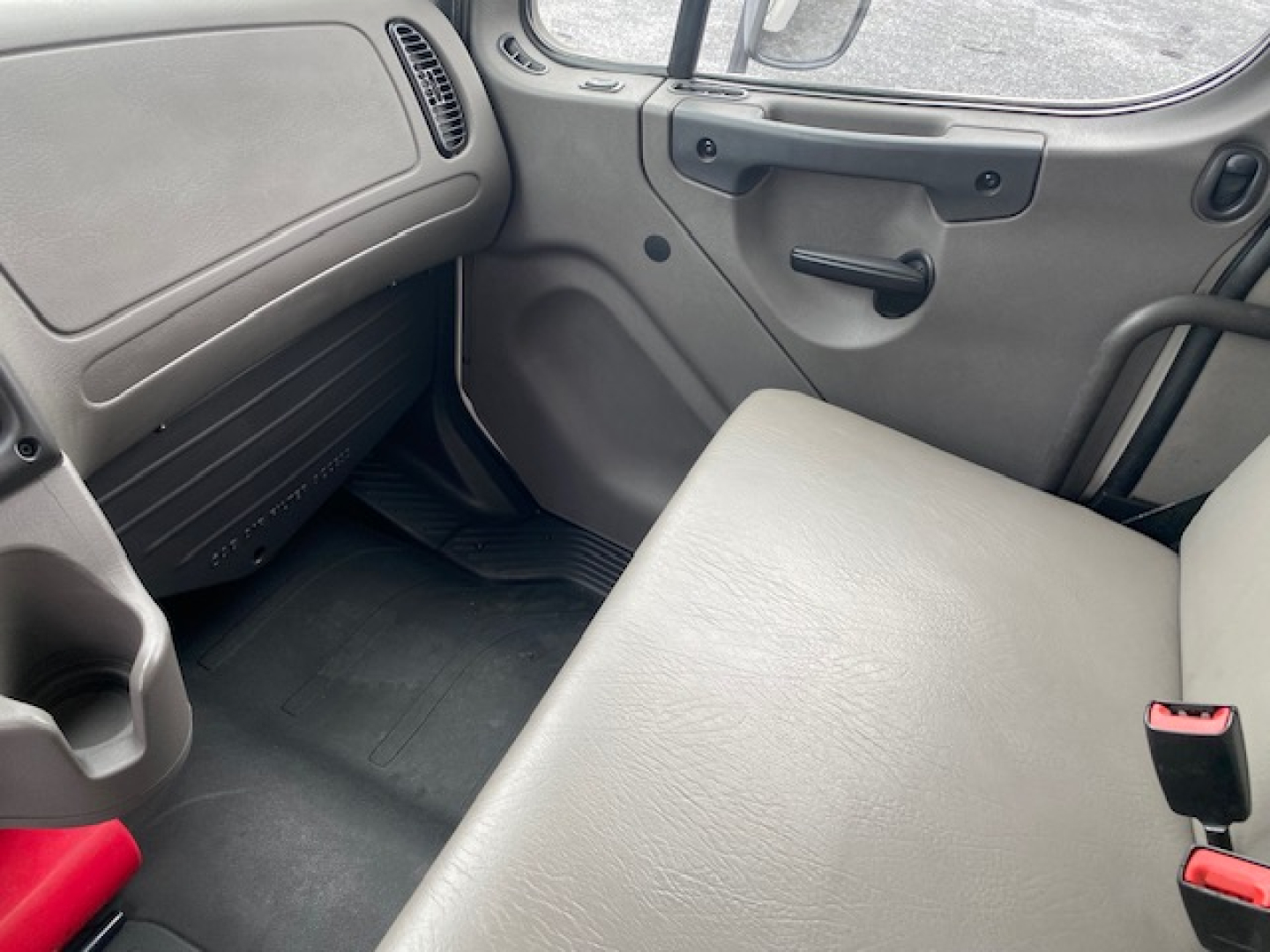 Cab interior of a Freightliner M2-106 truck showing gray bench seat, door panel with handle, and dashboard area.