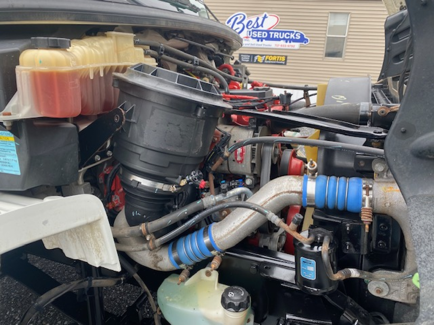 Engine bay of a 2019 Freightliner M2-106 showing coolant reservoir, hoses, and filter housing.