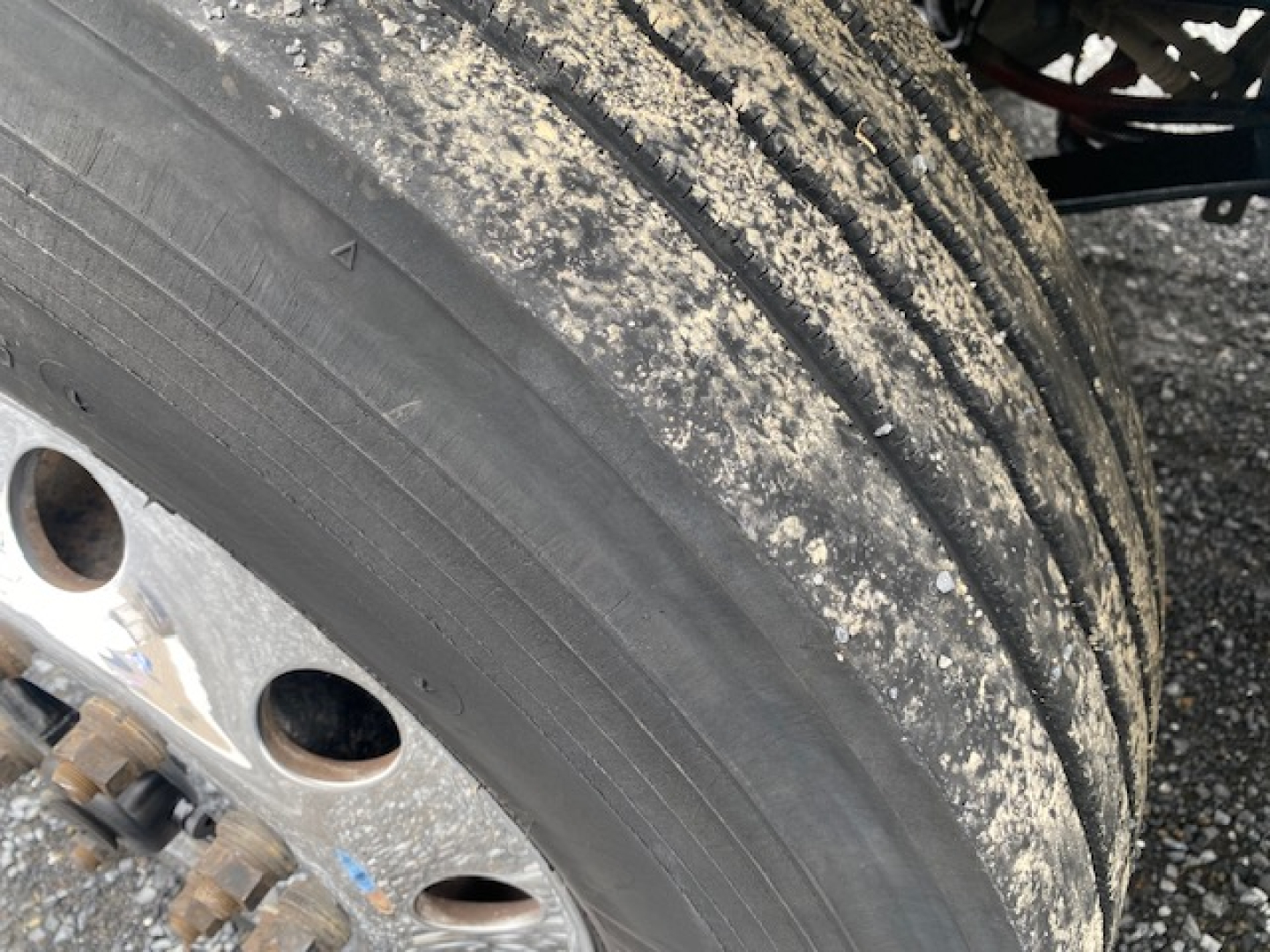 Freightliner M2-106 wheel and tire with dirt on tread and rim, part of truck chassis visible