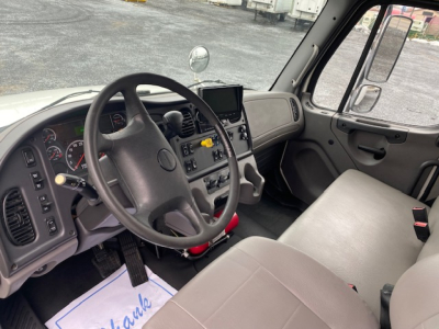 Cab interior of Freightliner M2-106 showing steering wheel, dashboard, and gray seats.