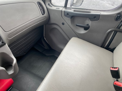 Cab interior of a Freightliner M2-106 truck showing gray bench seat, door panel with handle, and dashboard area.