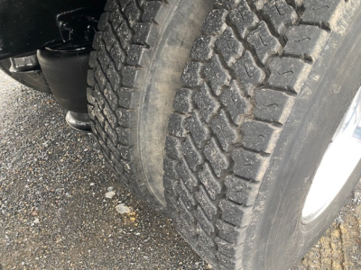 Truck front dual tires and wheel well showing tread pattern and suspension component in service condition.