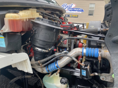 Engine bay of a 2019 Freightliner M2-106 showing coolant reservoir, hoses, and filter housing.