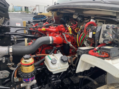 Freightliner M2-106 engine bay with red intake manifold, white reservoir, and various colored hoses and wires visible.