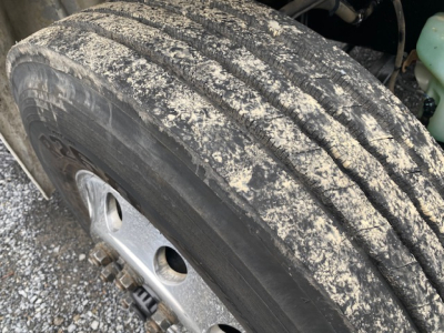 Truck wheel and tire close-up showing tread with dust and dirt on the Freightliner M2-106 component bay.