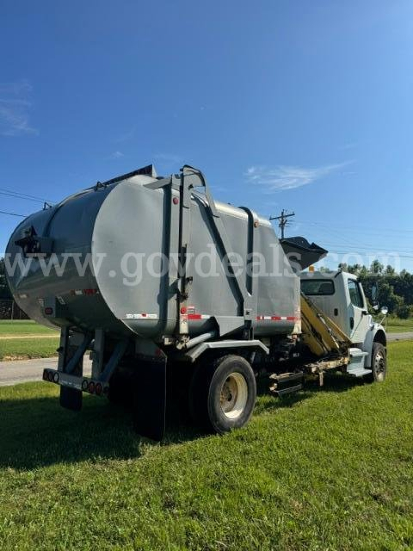 Truck-mounted vacuum tank tanker on a Freightliner M2 with rear view showing cylindrical tank and hoses.