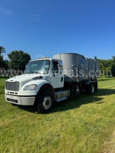Truck side view showing 2013 Freightliner M2 with a large waste hopper on a grassy field.