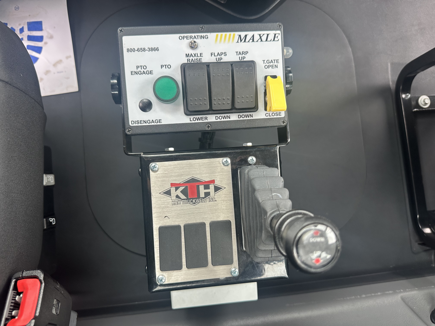 Control panel of a 2026 Mack GR64F dump truck showing MAXLE operating controls, green PTO engage button, yellow throttle/clip, and a KMH hydraulic control box with a textured metal plate.