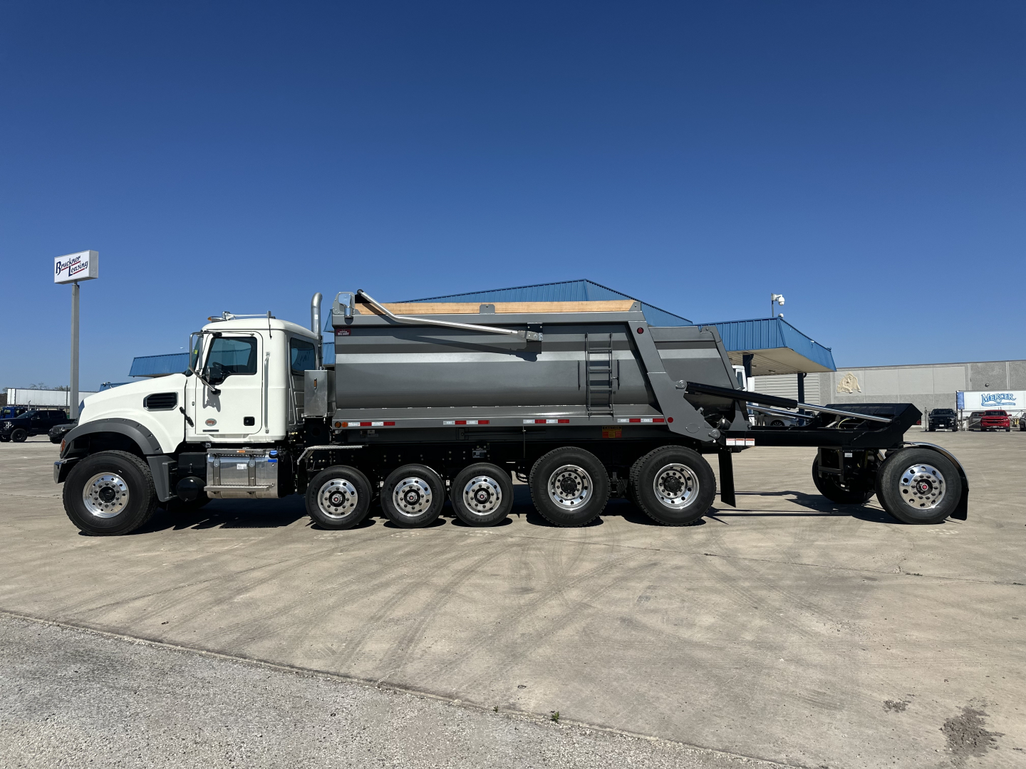 Dump truck chassis showing a white cab and gray dump body on a 6x4 with multiple axles and a rear-mounted dumping bed.
