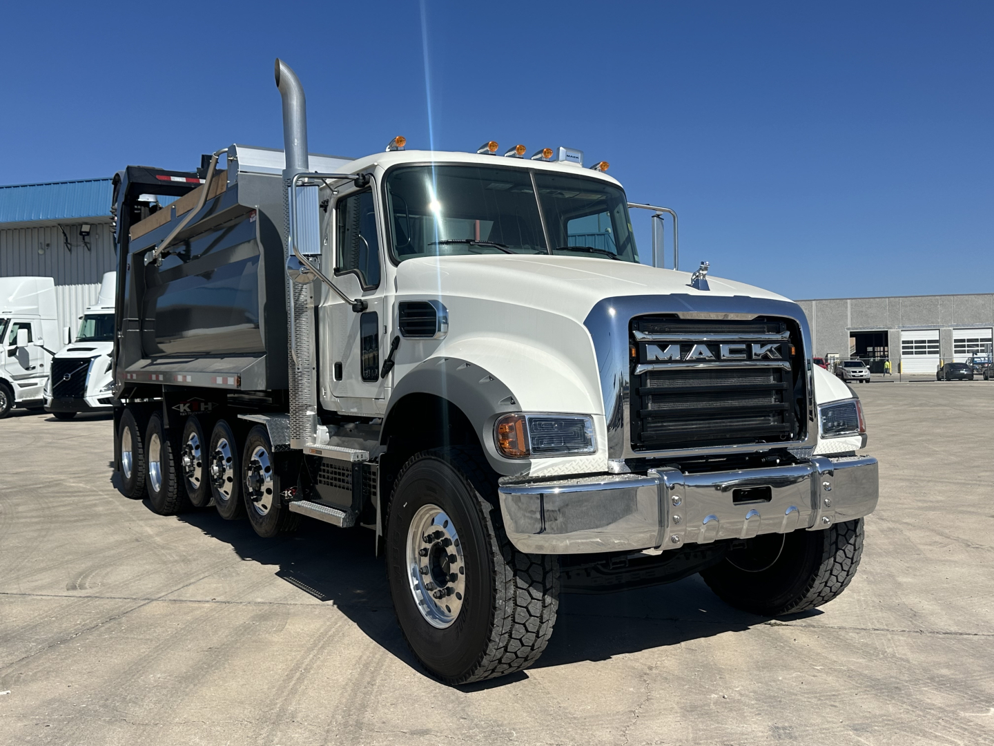 Mack GR64F dump truck showing front grille with MACK badge and chrome bumper, dual exhaust stacks, and dump bed.