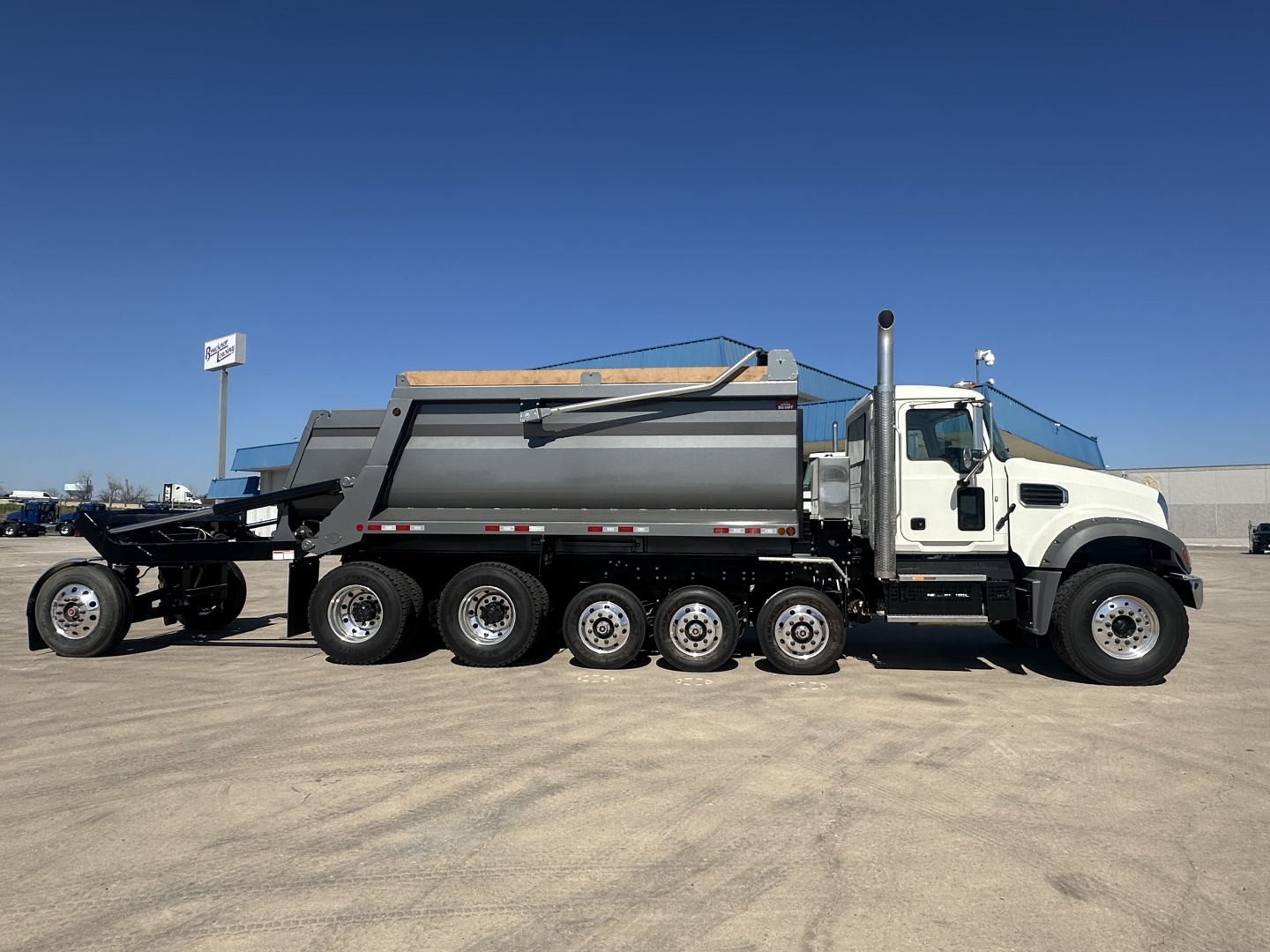 Mack GR64F dump truck side view showing multiple axles and gray dump body with white cab.