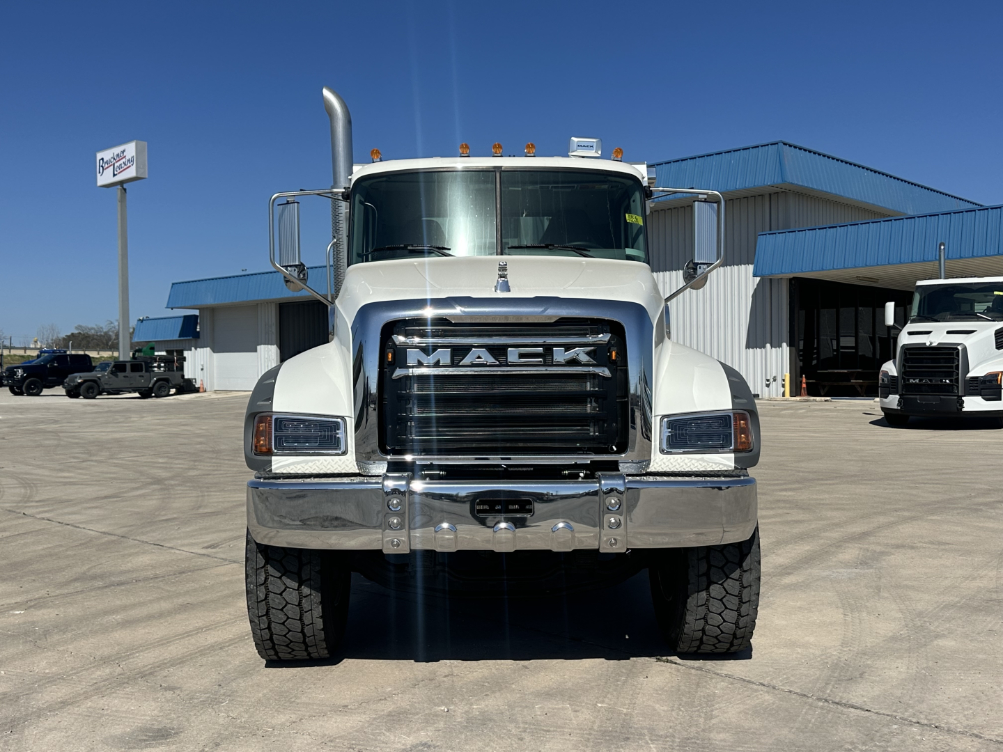 Mack GR64F dump truck front view showing large chrome grille with MACK lettering and bumper, heavy-duty tires, clear windshield, and side mirrors.