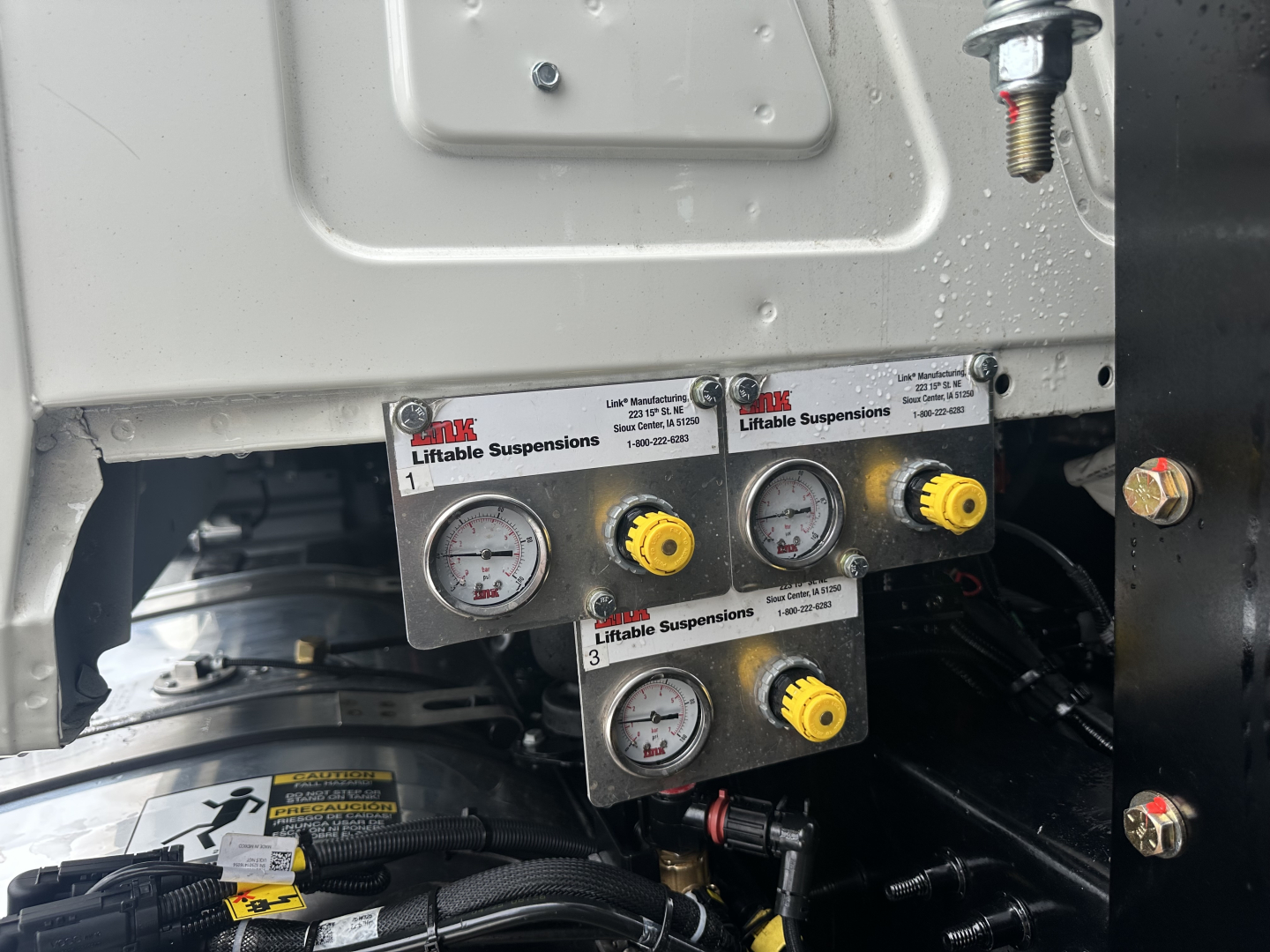 Panel with dual pressure gauges and yellow adjustment knobs mounted on Mack GR64F chassis, showing ‘Liftiable Suspensions’ branding on the label.