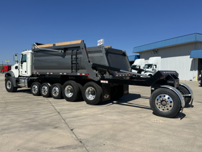 Dump truck with multiple axles and a dumping bed, side view showing Mack GR64F chassis and hydraulic dumping mechanism.
